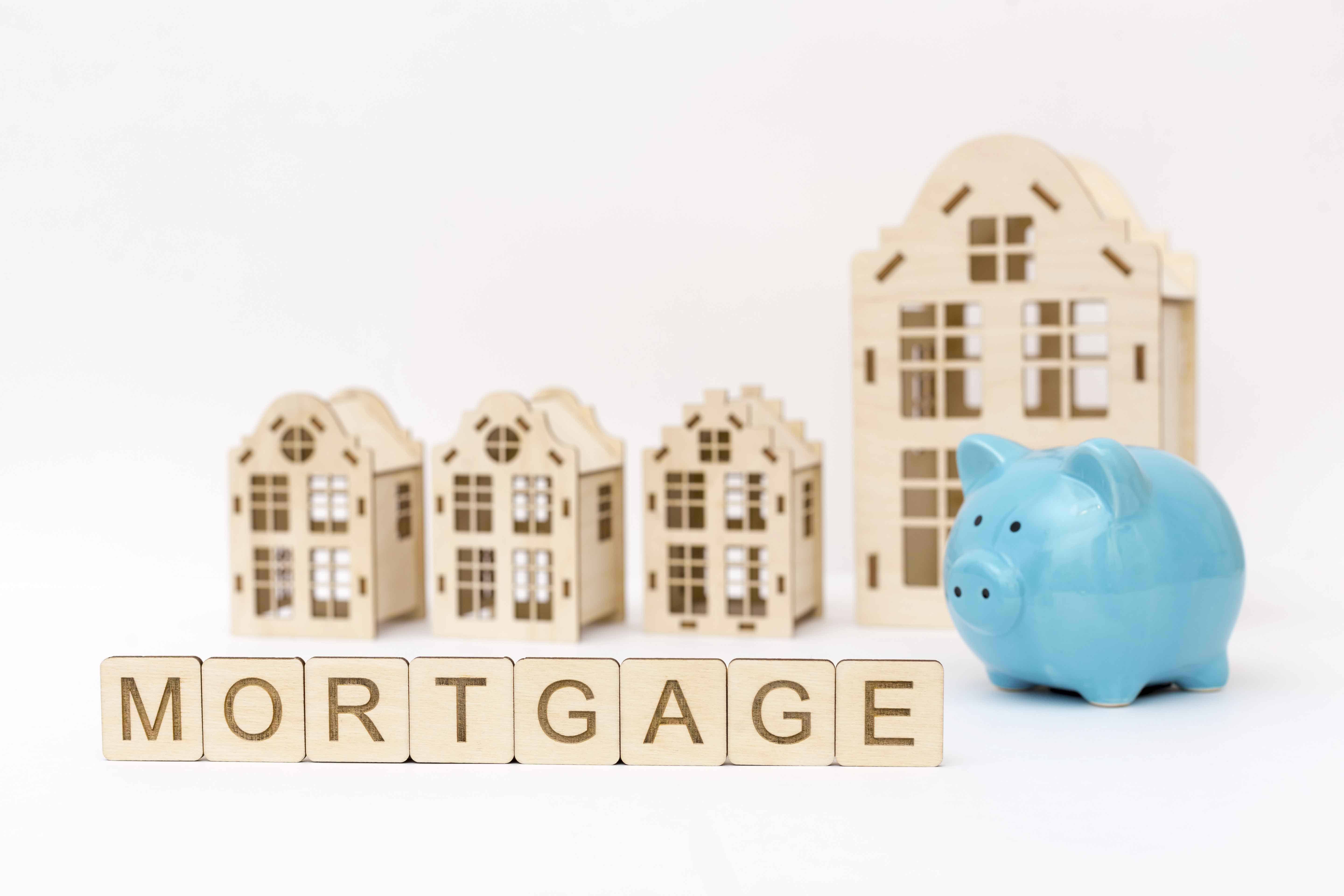 Blue piggy bank and wooden sign "mortgage" house model on background