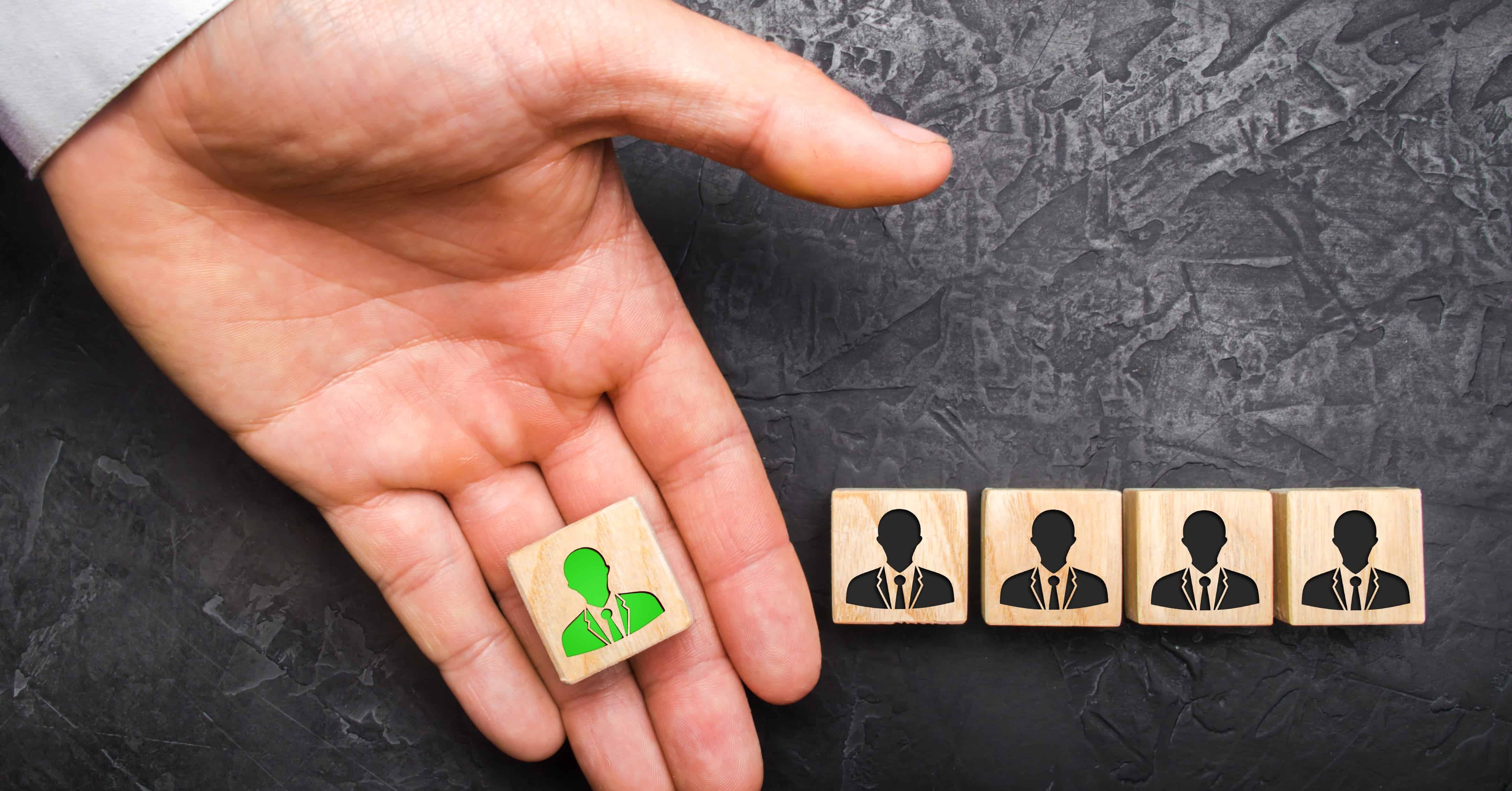 A hand holds out a green leader figure to a team of employees. Headhunter recruits staff and business personnel management. The concept of finding Specialists and workers on the job.