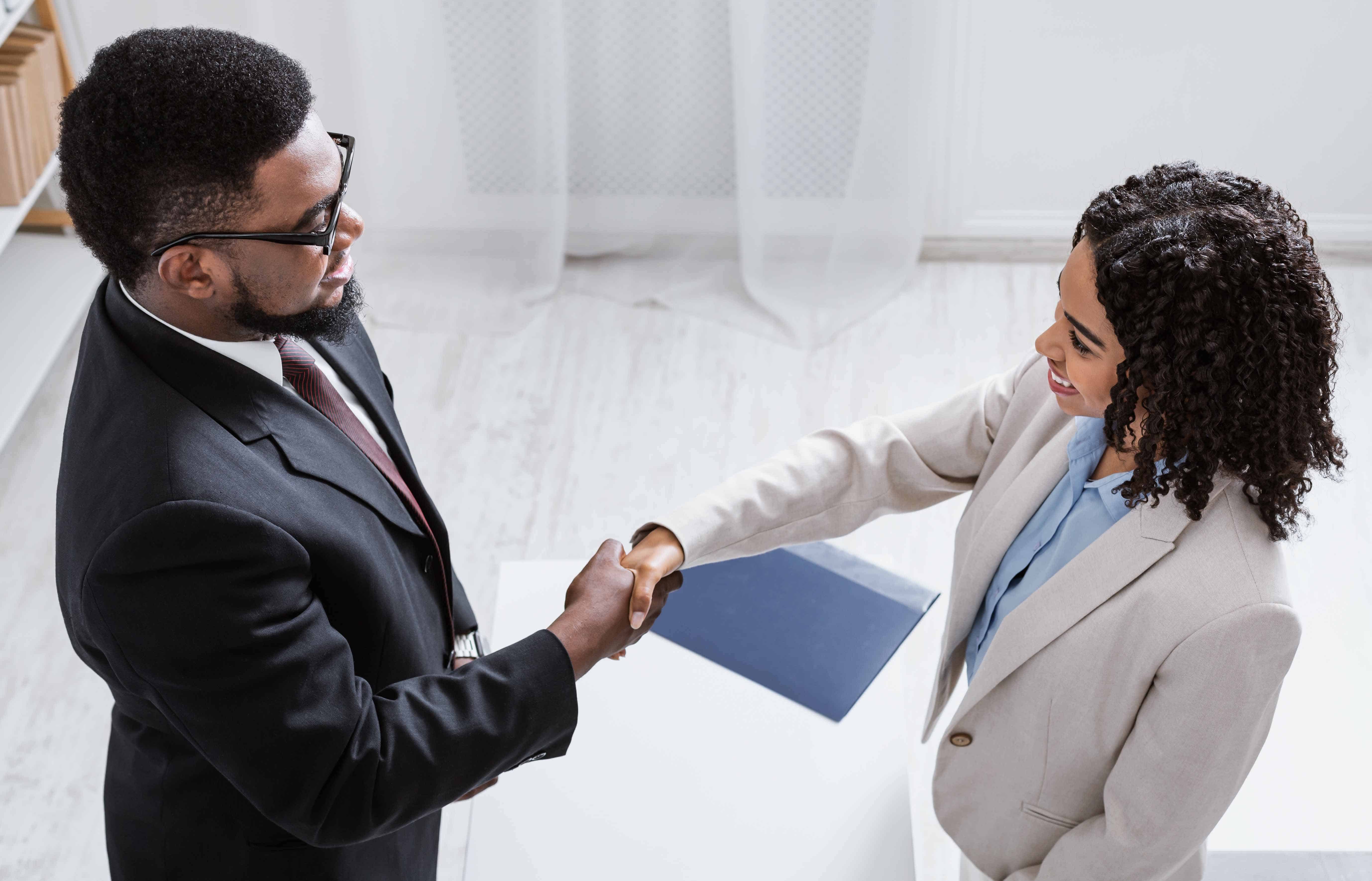 Human resources manager shaking hands with successful vacancy applicant at office, above view. Career fair concept