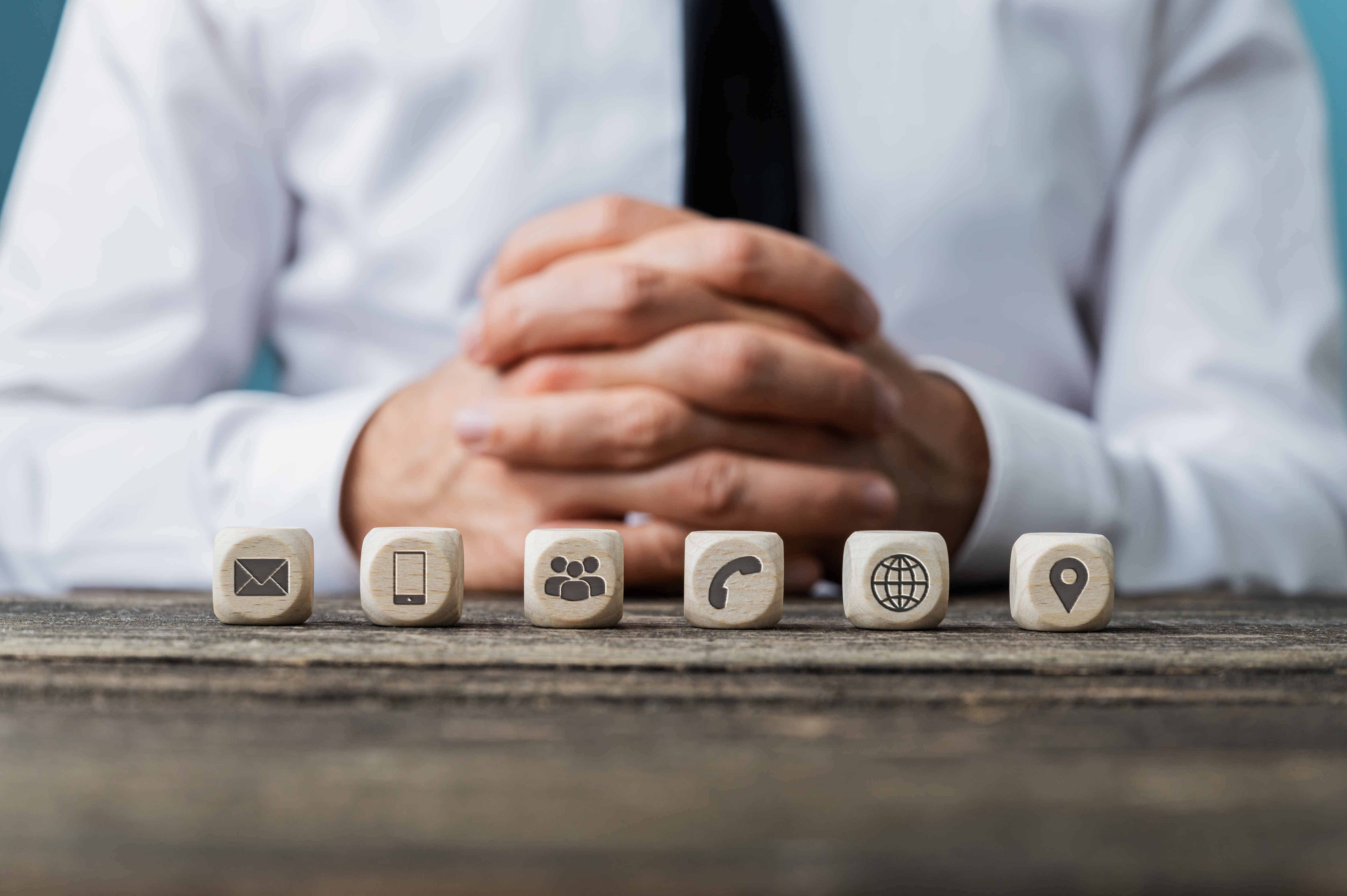 Customer service and help concept - business operator sitting at rustic wooden desk with six dices with contact and information symbols on them placed in a row.