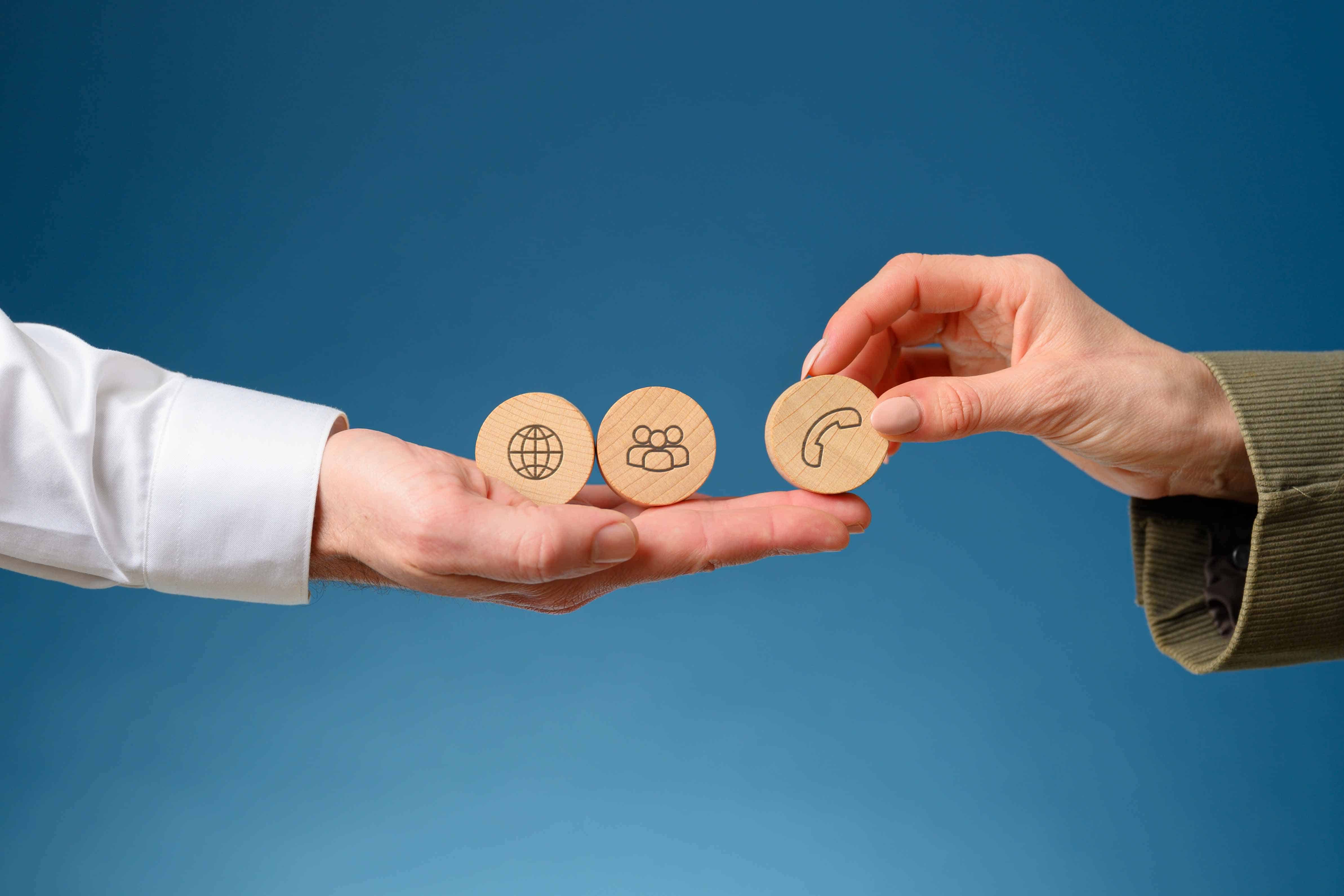 Female hand placing three wooden cut circles with contact and communication icons on them on a businessmans hand.